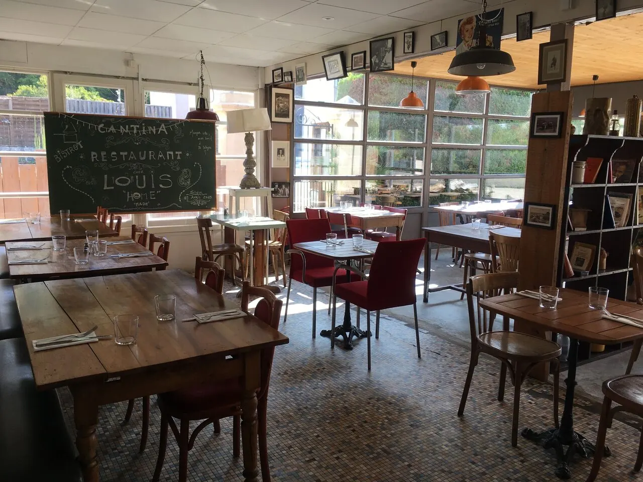 La salle du bistrot : tables en bois, chaises bistrot, ardoise et cadres aux murs